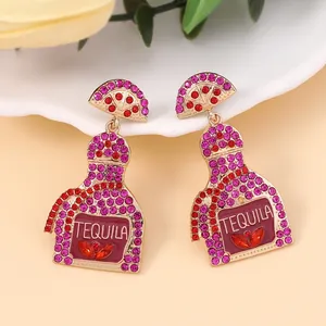 Detailed view of gold alloy Tequila bottle earrings with pink rhinestones and citrus charm