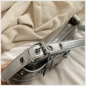 Detail of silver metallic Y2K shoulder bag featuring wide strap with metal eyelets and buckle