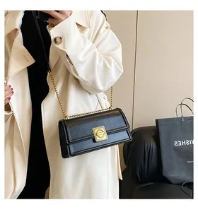 Detail of elegant black PU leather square bag with gold lock and chain strap on trench coat
