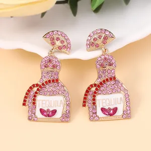 Macro view of gold tequila bottle earrings with pink rhinestones and lemon slice stud detail