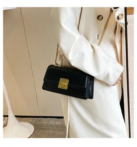 Close-up of black leather chain bag with gold lock worn on a beige trench coat