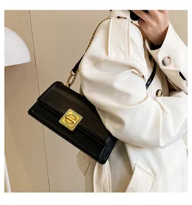 Detail of black rectangular crossbody bag with golden square lock and metal chain strap