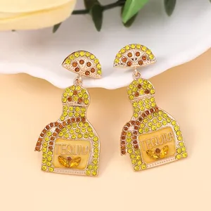Close-up of golden Tequila bottle earrings with yellow rhinestones and lemon slice detail