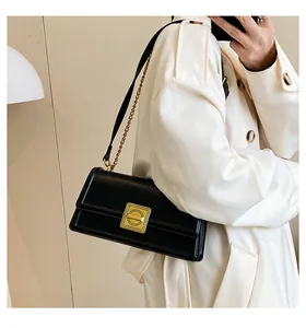 Detail of a black leather crossbody bag featuring a golden square metal clasp and chain strap
