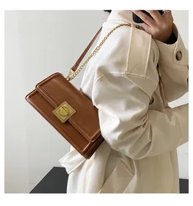 Detail view of brown PU leather shoulder bag with golden lock and chain strap on model