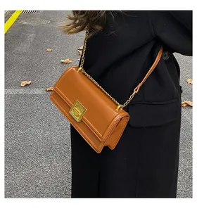 Tan leather crossbody bag with gold square metal buckle and chain strap on a model