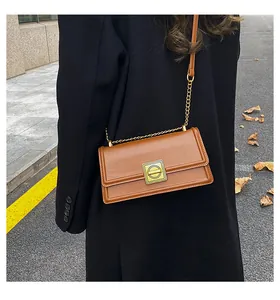 Close-up of a vintage brown leather square bag with gold buckle and chain strap on a coat