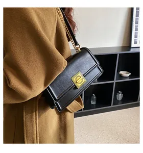 Detail of black glossy leather shoulder bag with gold square buckle and chain strap on model