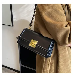 Detail of black faux leather crossbody bag with matte gold square rotary lock and chain strap