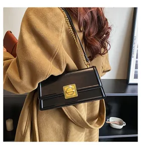 Detailed view of black patent leather square bag with vintage gold buckle on camel coat