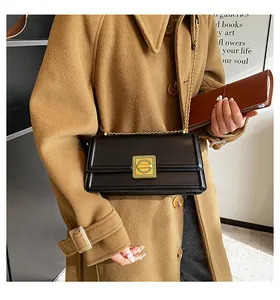 Macro detail of the black leather bag featuring a gold square buckle and chain strap