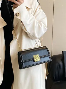 Classic black leather-textured crossbody bag with golden chain strap on a trench coat