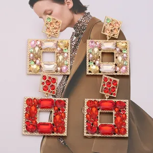Macro detail of geometric square drop earrings with colorful crystals on a magazine background