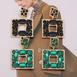 Close-up of geometric gold earrings with black and emerald green faceted crystals