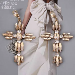 Close-up van oversized goudkleurige kruisoorbellen met marquise en ronde strassteentjes
