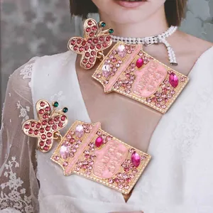 Detail of pumpkin spice cup earrings featuring pink rhinestones and a gold butterfly