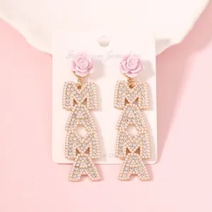 Macro detail of MAMA letter earrings with pink rose, pearls, and crystals on a card