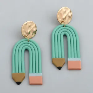 Macro detail of pencil-shaped clay earrings with hammered gold metal discs and pink erasers