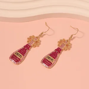 Detail of gold earrings shaped like champagne bottles with pink rhinestones and Cheers text