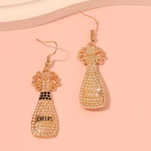 Close-up of champagne bottle earrings with white pearls and Cheers engraving