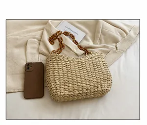 Detalle del bolso de paja trenzada con cadena de carey y comparación de tamaño con móvil