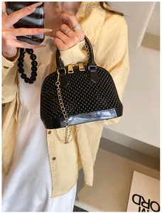Detail of a black beaded shell-shaped handbag with gold chain strap shown on model