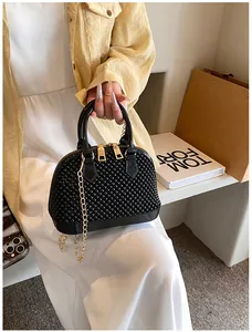 Detail of black beaded shell bag with gold chain strap held by a model in a street style