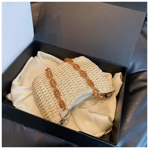 Detalle de bolso bandolera de paja con cadena de acrílico ámbar sobre raso blanco en caja
