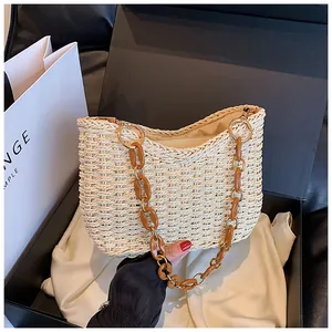 Detalle de bolso hobo de paja tejida con cadena acrílica marrón en caja de regalo