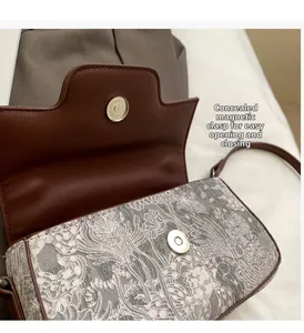 Detail of magnetic buckle closure on gray floral print crossbody bag with brown leather trim