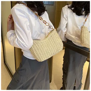 Detalle de bolso bandolera de paja con cadena de ámbar y textura tejida en un modelo