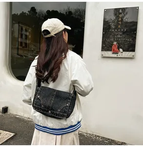 Détail d'un sac bandoulière en denim noir avec coutures apparentes et rivets en métal
