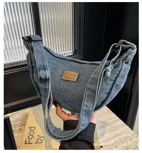Détail d'un sac demi-lune en denim bleu avec écusson en cuir marron et fermeture éclair