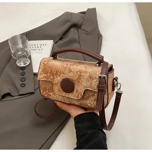 Detail of vintage textured crossbody bag with brown handle and orange-brown floral embossing