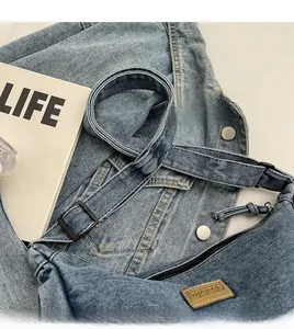 Détail de la bandoulière réglable avec boucle en métal sur le sac besace en jean bleu