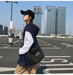 Detailed view of a black denim crossbody bag with white oval logo in an urban street setting