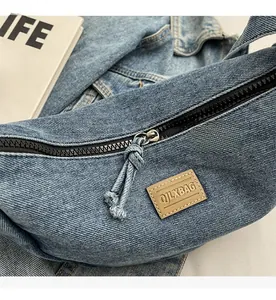 Détail du zip noir et du tirette tissée sur le sac bandoulière en jean bleu