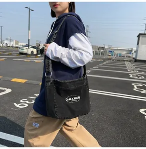 Close-up of black washed denim crossbody bag with adjustable wide shoulder strap on a model