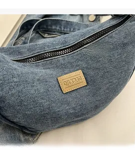 Détail rapproché du sac bandoulière en denim bleu avec tissu texturé et étiquette en cuir