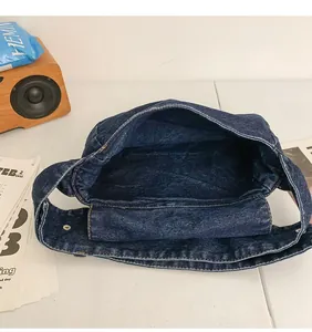Détail du sac bandoulière en denim foncé montrant l'espace intérieur et le bouton