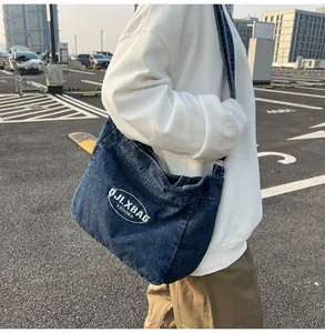 Detail of large denim crossbody bag showing white embroidery and adjustable strap on model