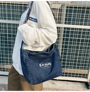 Outdoor lifestyle shot of a large dark blue denim crossbody bag with white oval logo