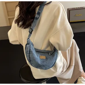 Vue détaillée du sac croissant en denim avec étiquette en cuir marron et bandoulière réglable