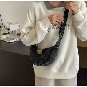 Détail d'un sac demi-lune en denim délavé noir avec écusson en cuir dans un café