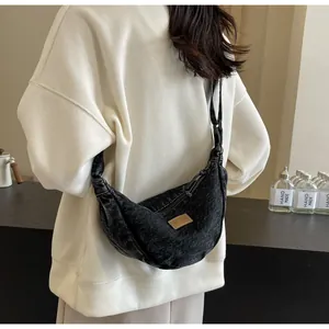 Détail du sac croissant en denim noir avec bandoulière réglable et écusson logo carré