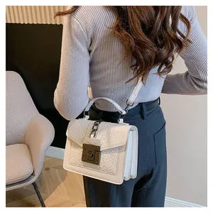 Detail einer weißen Handtasche mit Krokodilprägung und Metallschnalle am Modell