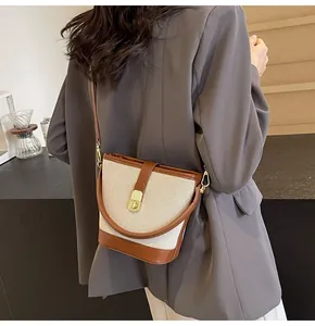 Detail view of a canvas and brown leather bucket bag styled on a model in a warm setting