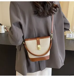 Detail of a beige canvas handbag with brown leather trim and golden logo buckle on a model