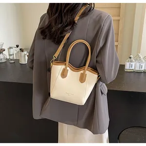 Detail of a wave-edge tote bag in beige and brown with golden metal hooks and logo