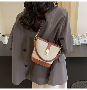 Detail of beige canvas and brown leather crossbody bucket bag with gold clasp